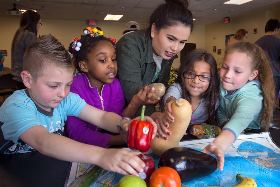 Young students and their teacher place colorful vegetables on a map.